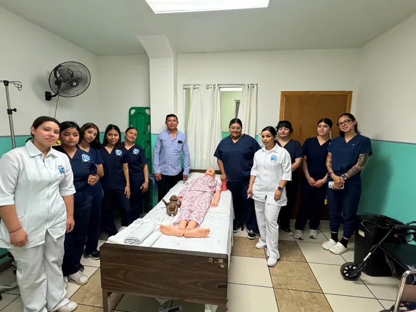 Grupo de CIMAC Tecate en el laboratorio de prácticas, junto a la cama con maniquí
